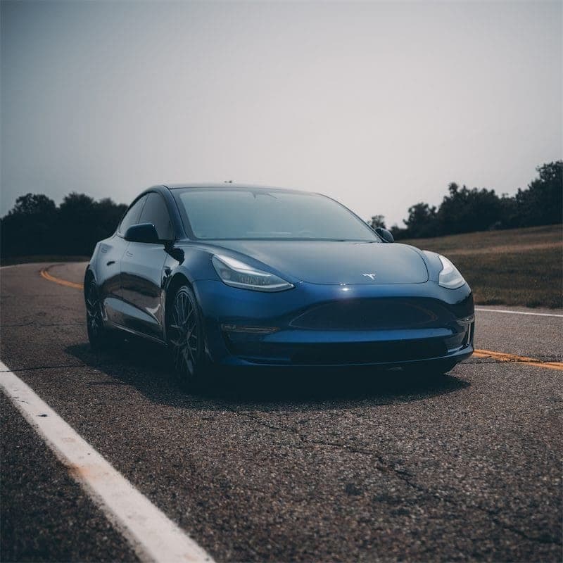 Front three-quarter view of the blue Model 3 on a curving road with yellow centre lines.